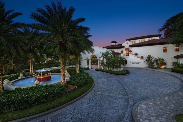 A courtyard with a fountain, palm trees, and a building labeled 'CASA BENEVENUTO.'