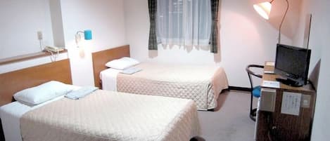A hotel room with two beds, a desk with a computer, a lamp, and a window with sheer curtains.
