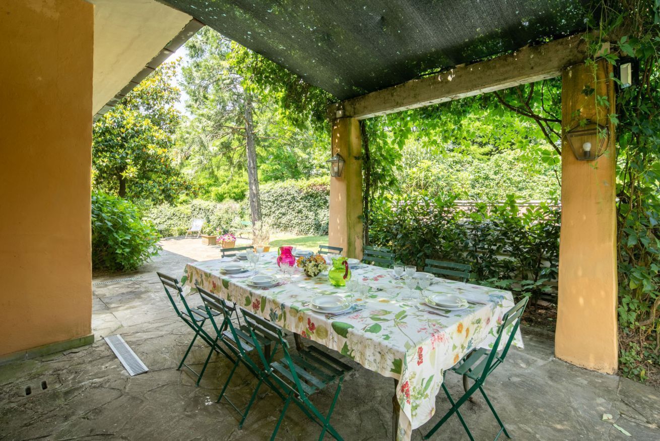 An outdoor patio with a table set for dining, surrounded by greenery.