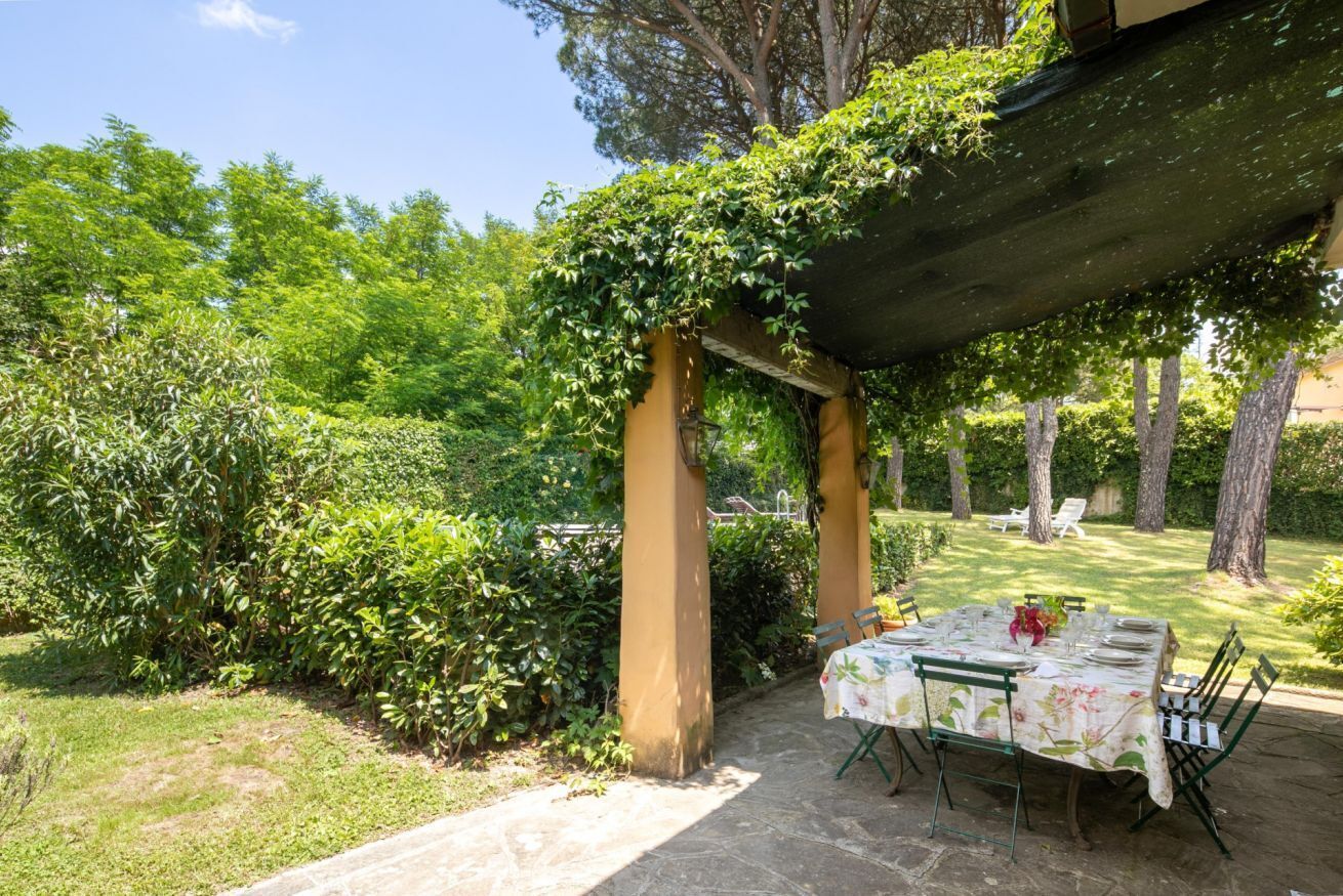 Une terrasse extérieure couverte, avec une table dressée pour les repas, entourée d’une végétation luxuriante et d’arbres.