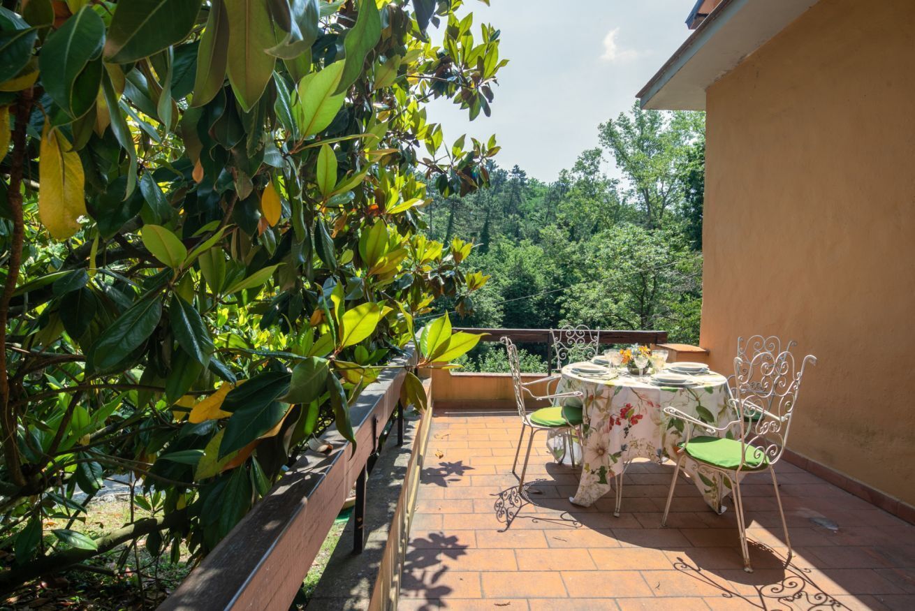 An outdoor patio with a table and chairs, surrounded by greenery and a view of trees.