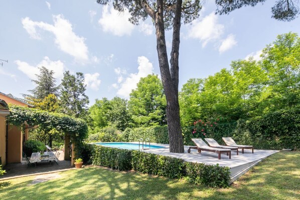 A backyard with a swimming pool, lounge chairs, and a pergola.