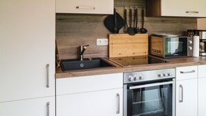 Cozinha moderna com fogão, forno e micro-ondas embutidos. Possui bancada de madeira e pia com torneira.