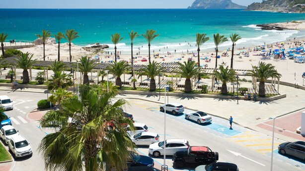 Een parkeerplaats aan het strand met auto's, palmbomen en uitzicht op het strand en de oceaan.