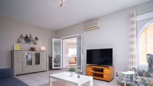 Een moderne woonkamer met een bank, een televisie, een kast en een eettafel.