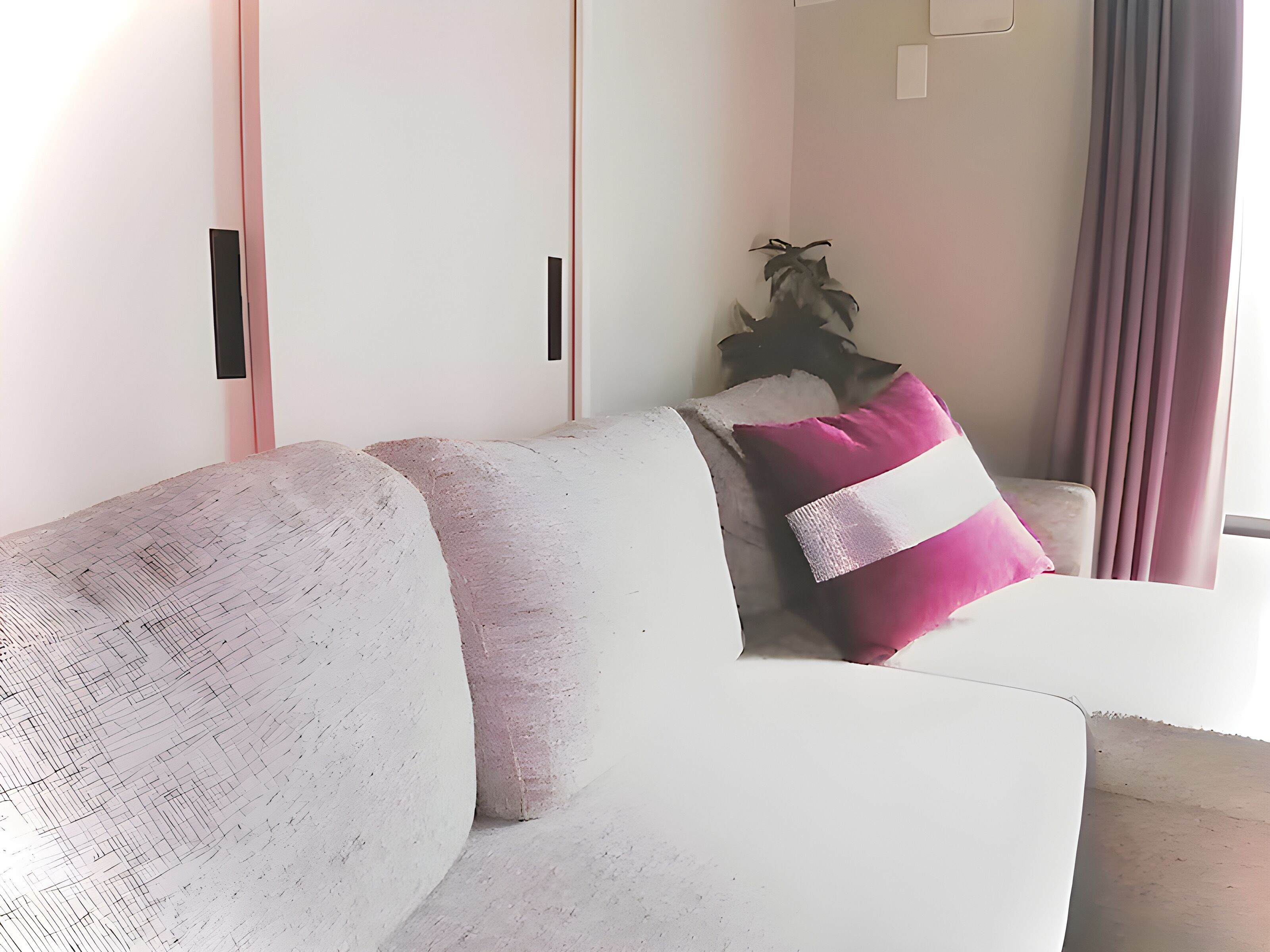 Uma sala de estar moderna com um sofá branco, uma almofada rosa e uma planta.