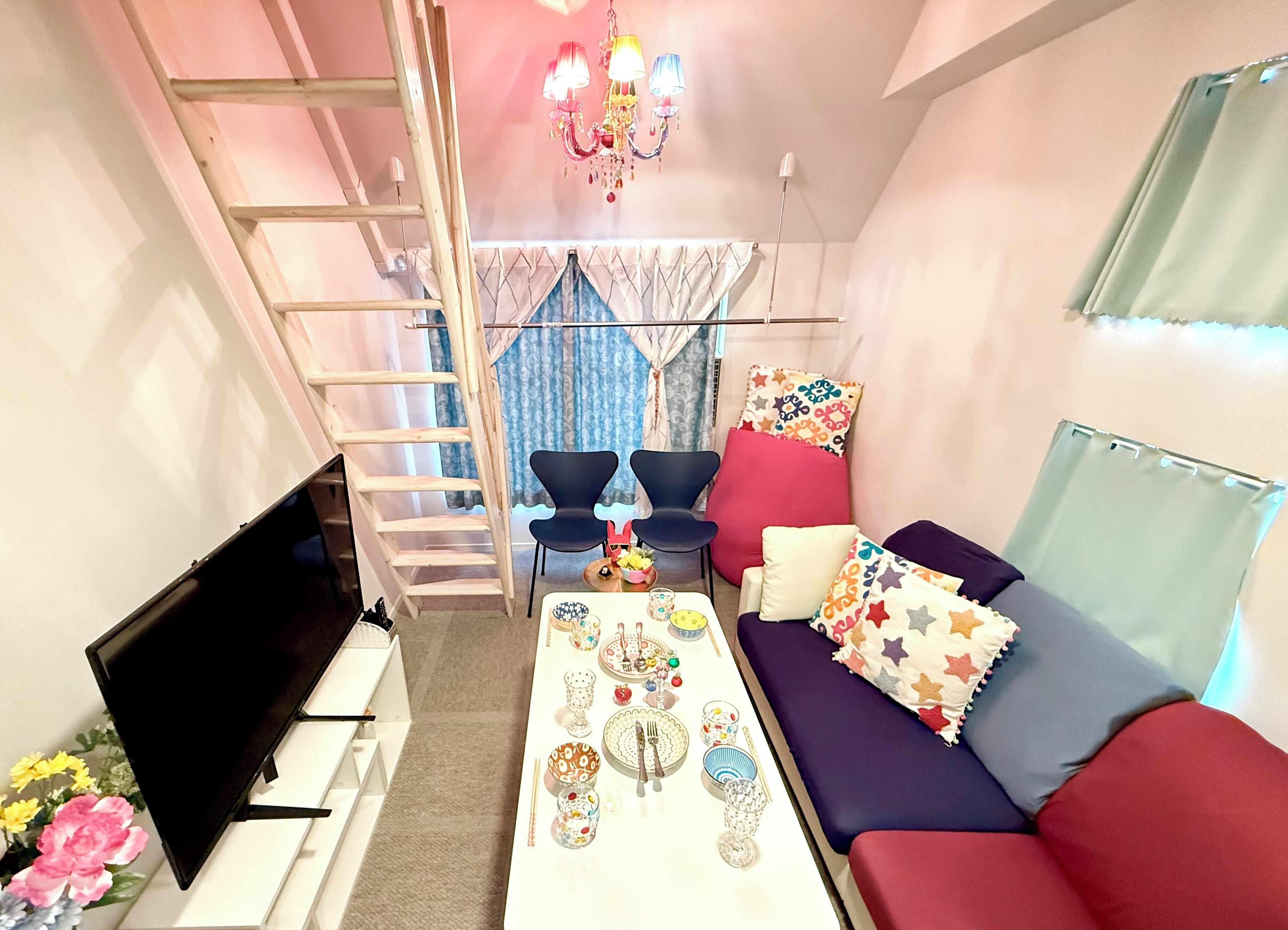 A compact living space with a sofa, chairs, a coffee table, a TV, a ladder, and a chandelier.