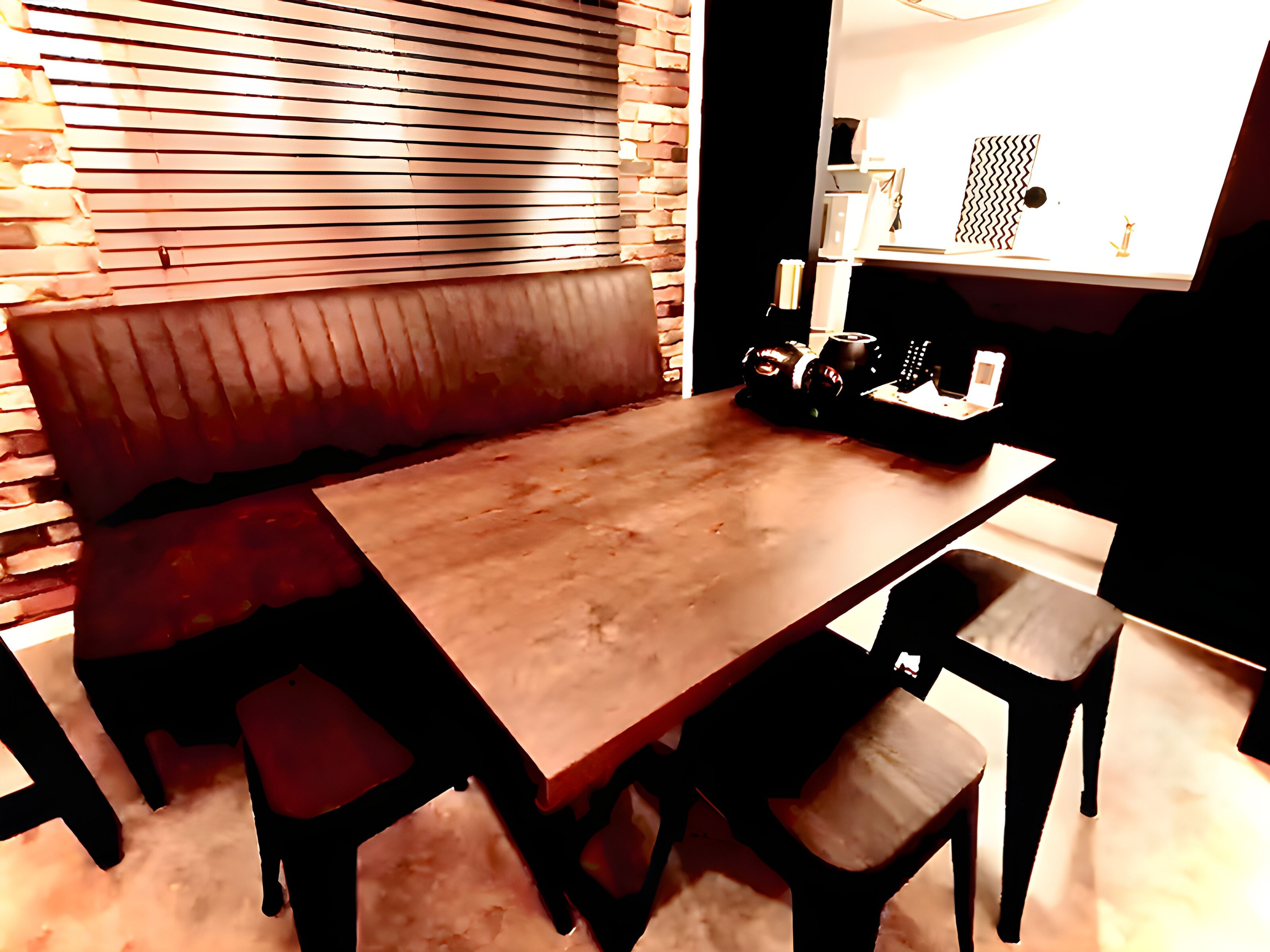 Un comedor con una mesa de madera y cuatro sillas, un banco a lo largo de una pared, y una pared de ladrillo con listones horizontales.