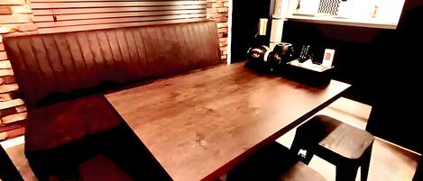 Un comedor con una mesa de madera y cuatro sillas, un banco a lo largo de una pared, y una pared de ladrillo con listones horizontales.