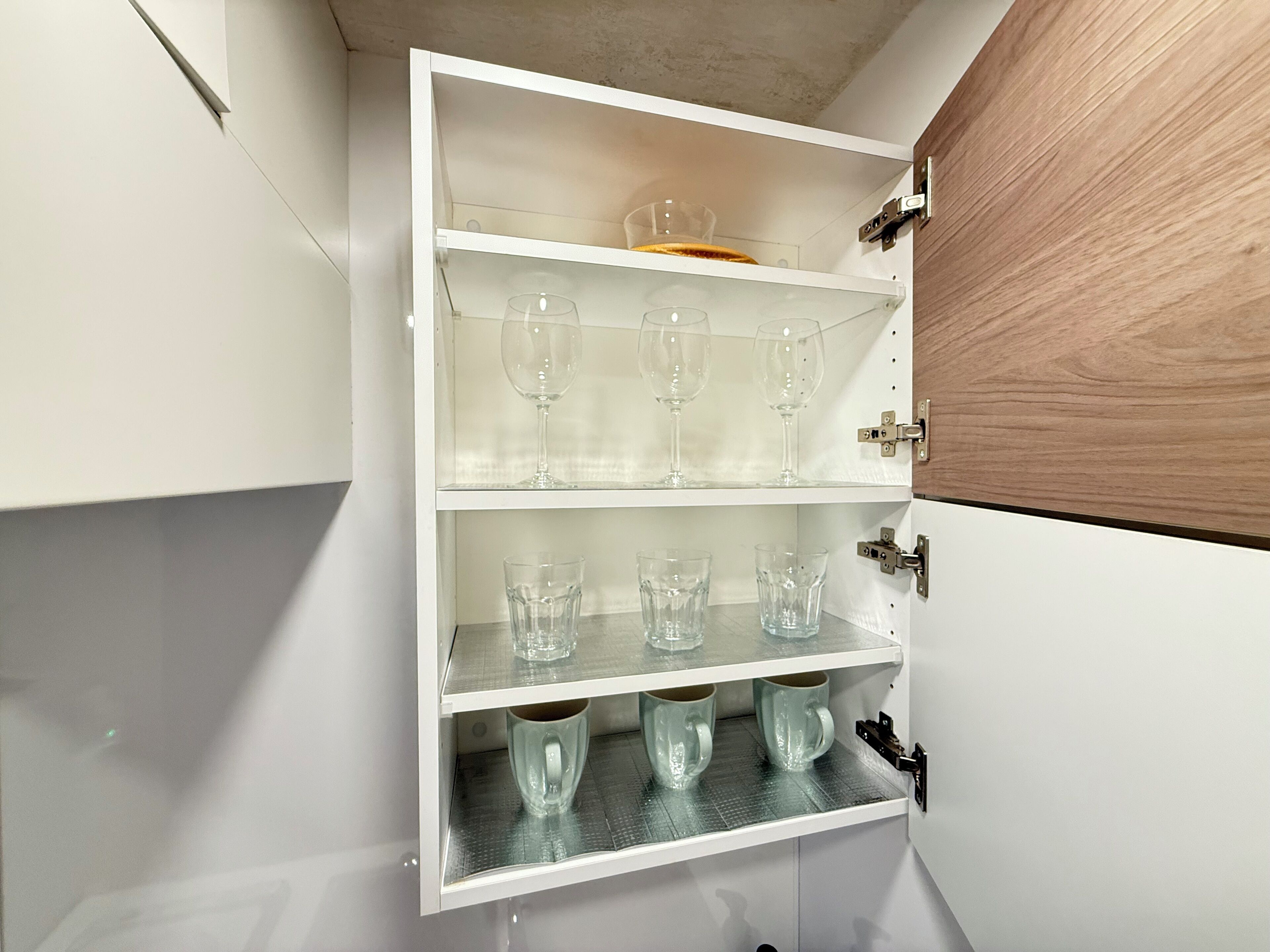 A white cabinet with three shelves, each holding clear glassware.