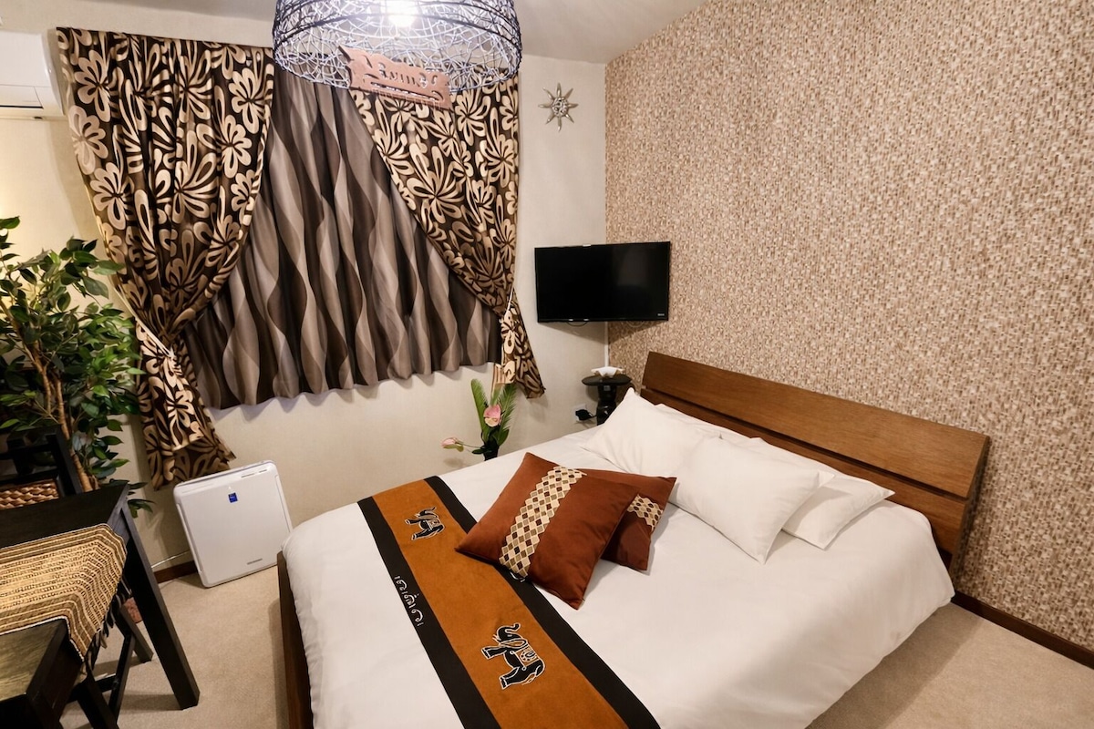 A hotel room with a bed, a TV, a desk, and a plant.