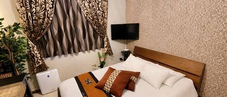 A hotel room with a bed, a TV, a desk, and a plant.