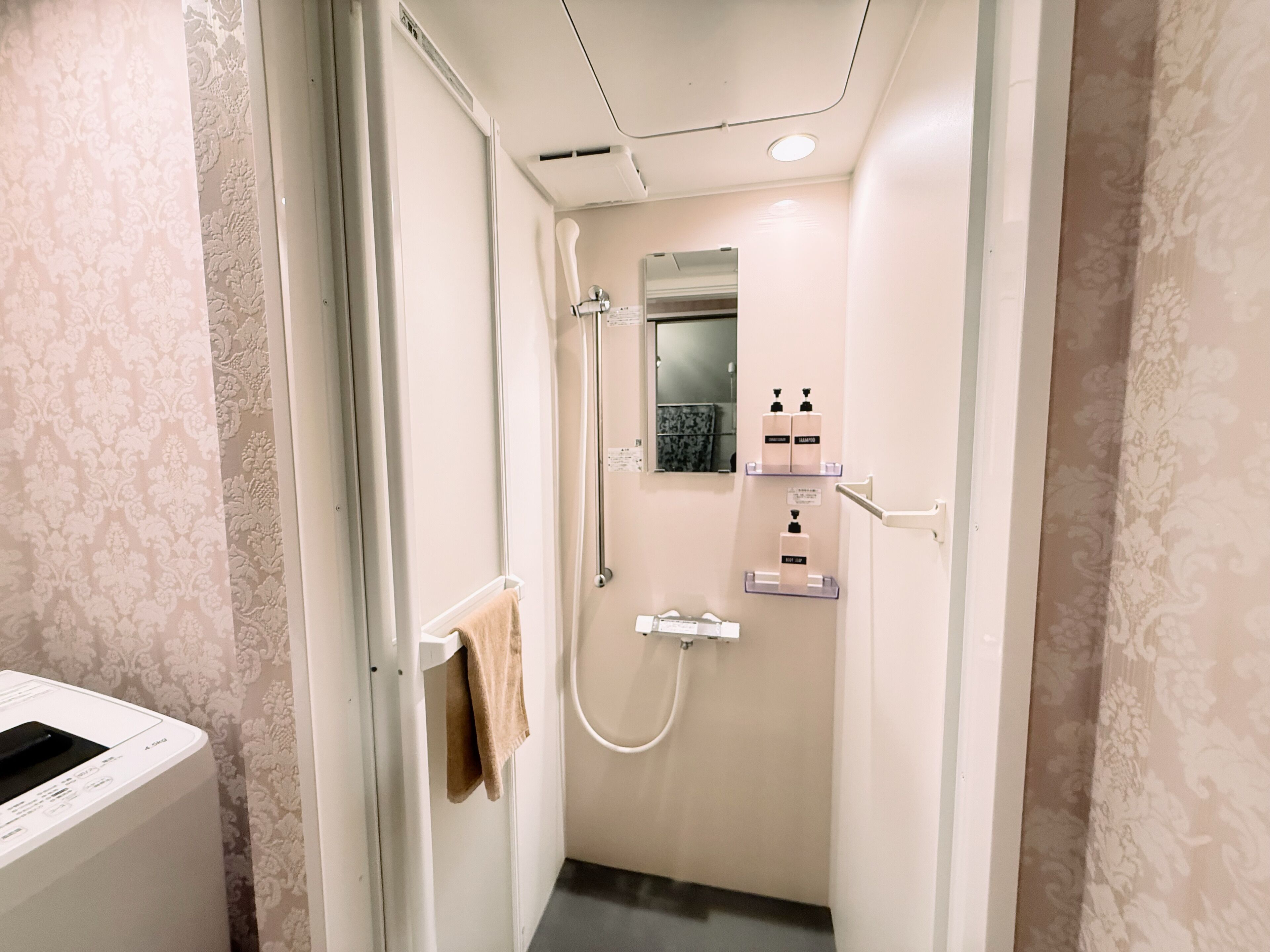 A small, well-lit bathroom with a shower, a towel rack, and a mirror.