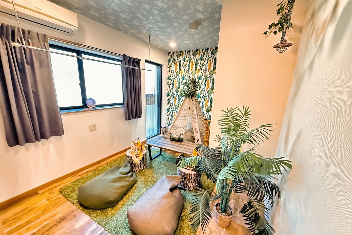 A cozy room with a large window, a small table, a chair, a tiger plush toy, and several potted plants.