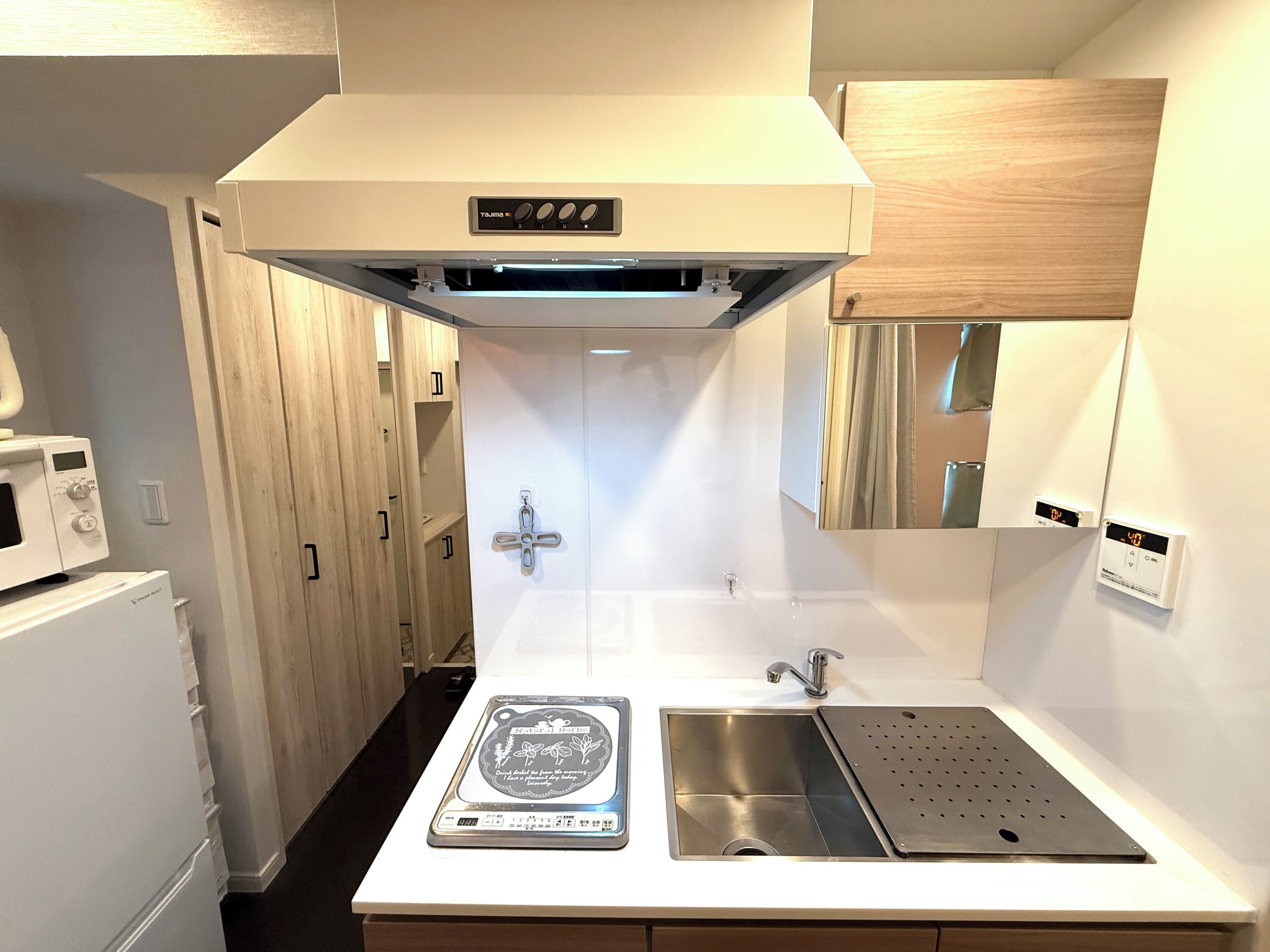 Uma cozinha compacta com micro-ondas, pia com cuba de aço inoxidável e coifa sobre o fogão.