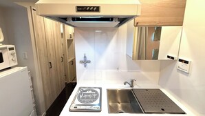 A compact kitchen with a microwave, a sink with a stainless steel basin, and a range hood above the stove. - Eternity APARTMENT HOTEL SHINAGAWA (Tokyo)