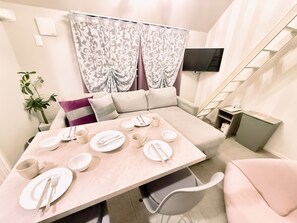 Una sala moderna con un sofá, una mesa de comedor con platos, tazas y cubiertos, una escalera, un televisor y una planta.