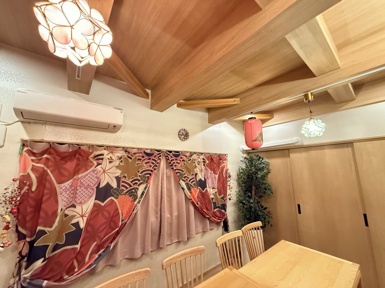 Una habitación con techo de madera, una mesa de comedor con sillas, un aire acondicionado instalado en la pared y una cortina decorativa.