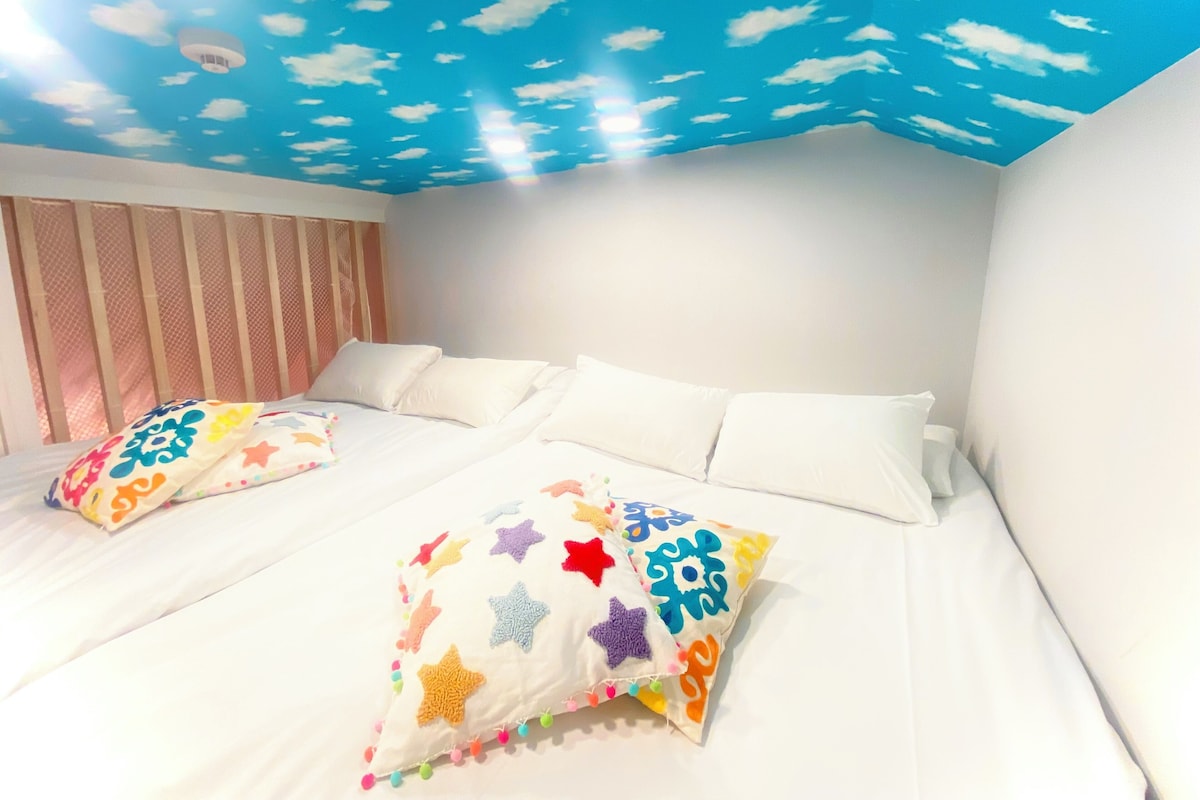 A room with a bed, pillows, and a ceiling with a cloud design.