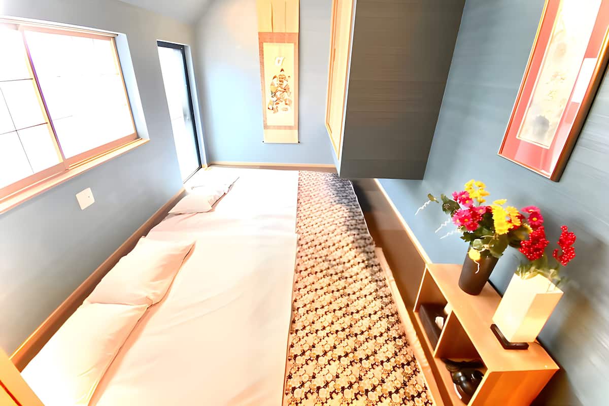 A hotel room with a bed, a window, a wall-mounted artwork, and a bedside table with a vase of flowers.