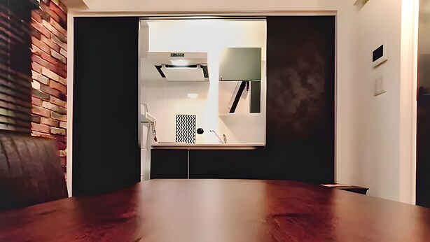 A modern room with a wooden dining table, a brick accent wall, and a kitchen area visible through an open door. - Eternity APARTMENT HOTEL SHINAGAWA (Tokyo)
