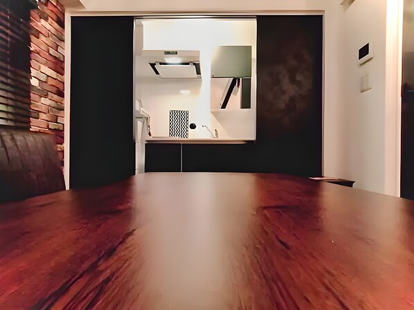A modern room with a wooden dining table, a brick accent wall, and a kitchen area visible through an open door. - Eternity APARTMENT HOTEL SHINAGAWA (Tokyo)