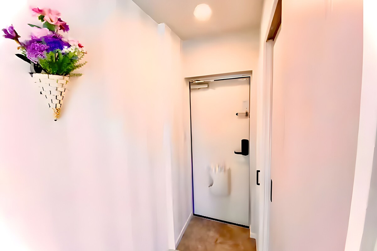 A hallway with a white door, a small step leading to a room, and a wall-mounted flower arrangement.