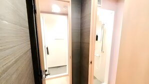 A hallway with a door leading to a bathroom. The bathroom has a shower area with a glass door. - Eternity APARTMENT HOTEL SHINAGAWA (Tokyo)