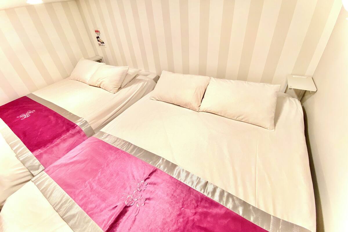 A hotel room with two beds, a striped headboard, and a pink decorative runner.