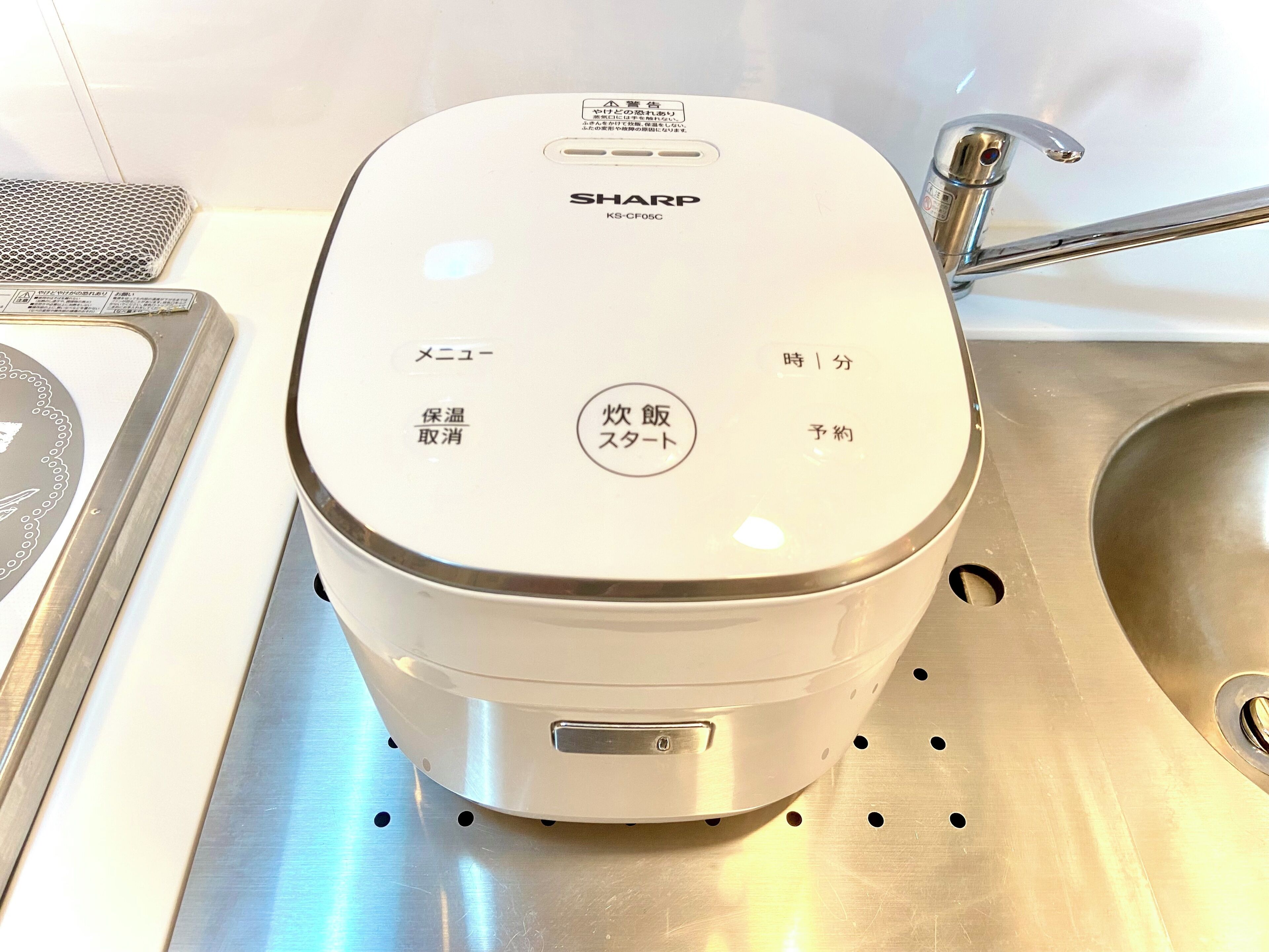 Una cocina con cafetera, pileta y superficie de malla metálica.