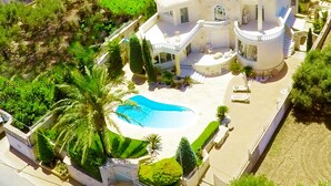 Vista aérea de una villa moderna con piscina, rodeada de exuberante vegetación y un jardín cuidado.