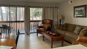 A living room with a leather sofa, a wooden coffee table, and a ceiling fan. There is a dining table with chairs and a window with curtains. - The Perfect Lie in Pinehurst! A golfer's paradise! (Pinehurst)