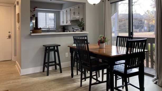 A modern kitchen with white cabinets, a dining area with a wooden table and chairs, and a large window with a view of the outside. - The Perfect Lie in Pinehurst! A golfer's paradise! (Pinehurst)
