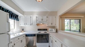 A compact kitchen with white cabinets, a stove, a microwave, and a dishwasher. - The Perfect Lie in Pinehurst! A golfer's paradise! (Pinehurst)