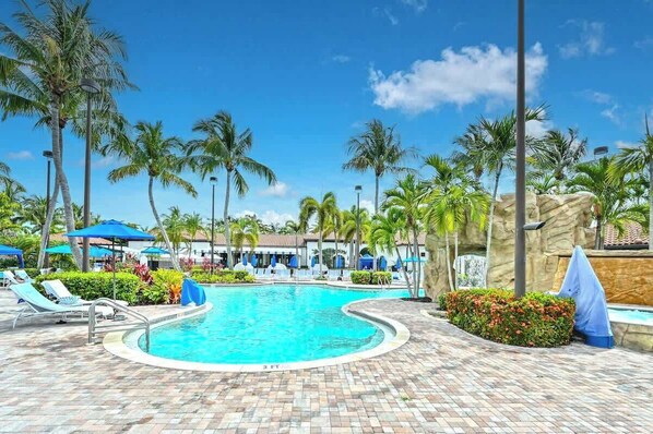 A pool area with lounge chairs, palm trees, and a clear blue sky.