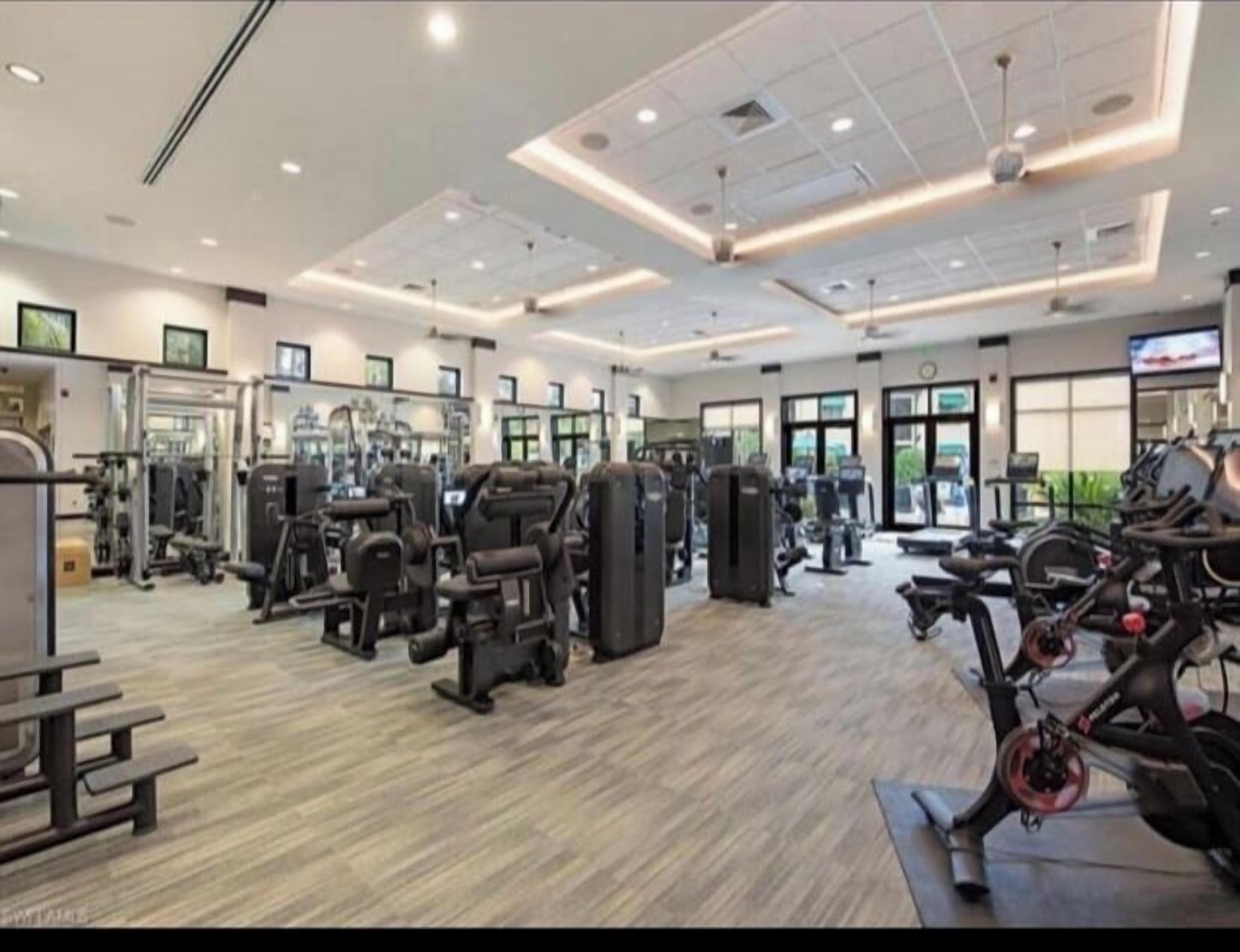 A modern gym with various exercise equipment, large windows, and a clean, well-lit interior.