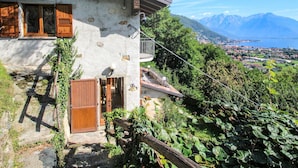 A rustic stone house with wooden shutters, a balcony, and a view of a lake and mountains. - Beautiful private villa for 6 people with WIFI, TV, terrace and pets allowed (Stazzona)