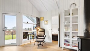 Un salon moderne doté d’une grande fenêtre, d’un fauteuil noir, d’un meuble blanc aux portes vitrées et d’un poêle noir.