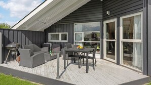 Un patio couvert avec des meubles d’extérieur, un barbecue et de grandes fenêtres.