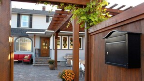 A covered patio with a wooden pergola, a red outdoor seating area, a barbecue grill, and a mailbox.