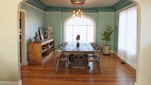 A dining room with a wooden table and chairs, a chandelier, and a large window.