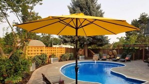 A swimming pool with a unique shape, surrounded by a wooden deck and a yellow umbrella.