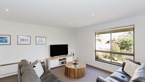 Una sala de estar moderna con un televisor de pantalla plana, una mesa de centro de madera y un ventanal con vistas a árboles.