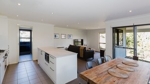 Una cocina moderna con una isla central, un área de comedor con una mesa de madera y una sala de estar con sofá y televisor.