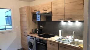 A modern kitchen with wooden cabinets, a built-in oven, a washing machine, a microwave, and a sink. - Rental house in Valras plage (34) 6/8 people (Sérignan)