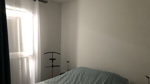 A bedroom with a bed covered in a patterned blanket, a standing lamp, and a floor lamp. - Rental house in Valras plage (34) 6/8 people (Sérignan)