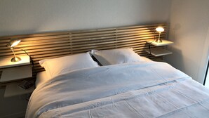 A neatly made bed with white linens, two bedside lamps, and a wooden headboard. - Rental house in Valras plage (34) 6/8 people (Sérignan)