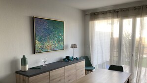 A modern dining area with a wooden table and chairs, a large abstract painting on the wall, and a view through sheer curtains to the outdoors. - Rental house in Valras plage (34) 6/8 people (Sérignan)