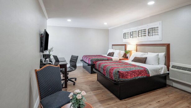 A hotel room with two beds, a desk, a chair, a TV, and a window with blinds. - Ritz Inn San Francisco SFO Airport (San Bruno)