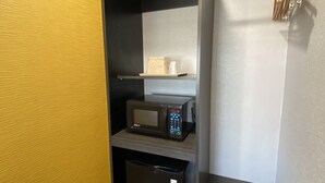 A compact kitchen with a microwave, a small refrigerator, and a shelf with a box. - Ritz Inn San Francisco SFO Airport (San Bruno)